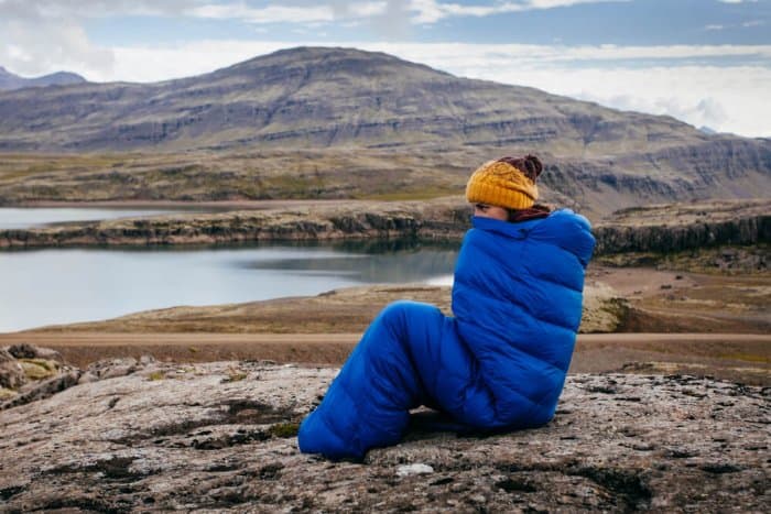 Woman staying warm in blue sleeping bag in Icelandic Highlands while camping