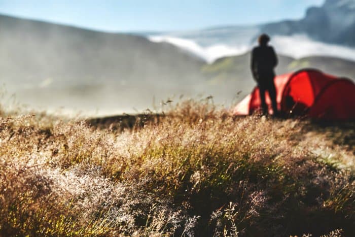 Man camping in Iceland standing next to his tent in Icelandic landscape