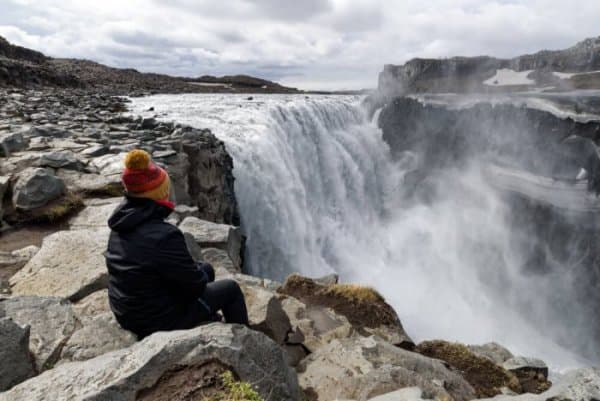 A female tourist sitting at the edge of Dettifoss waterfall