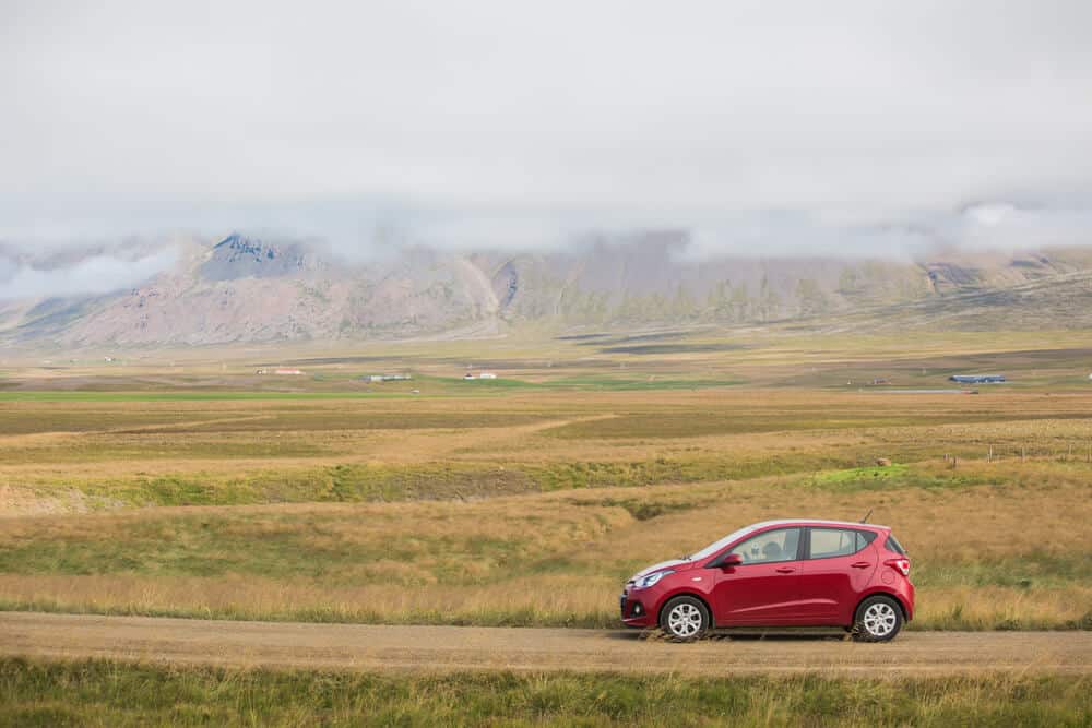 Red rental car in Iceland driving past beautiful landscapes