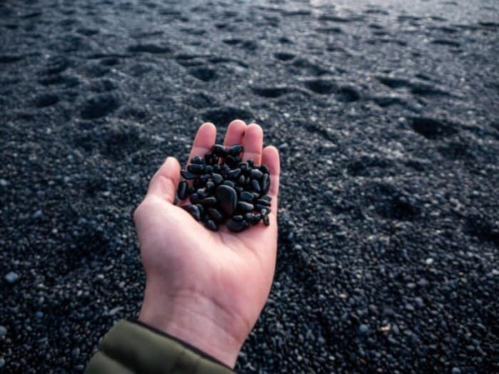 A men's hand full of pebbles from the black sand beach in Solheimasandur