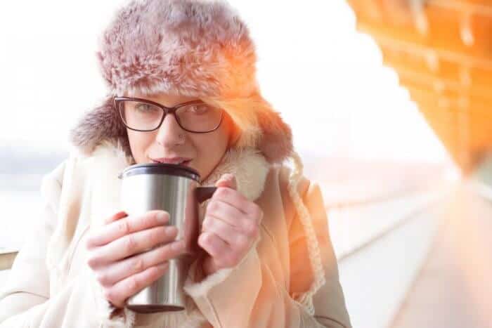 Woman with furry hat and coffee mug while camping in Iceland in November