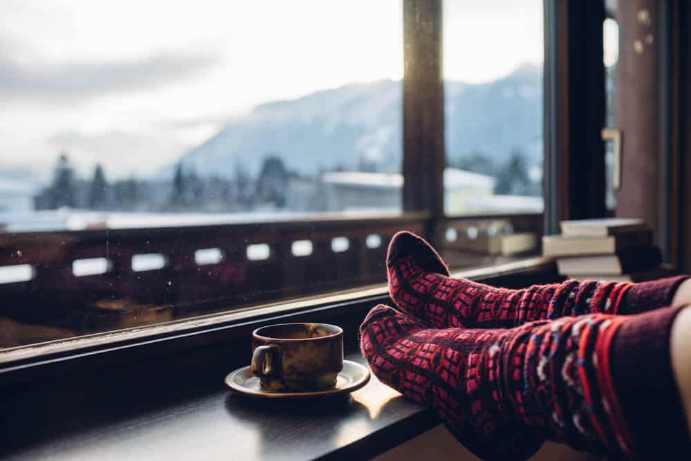 Woman sitting with fuzzy socks and coffee looking out over mountains