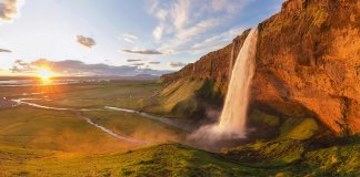 Midnight sun in Iceland on the horizon with a waterfall