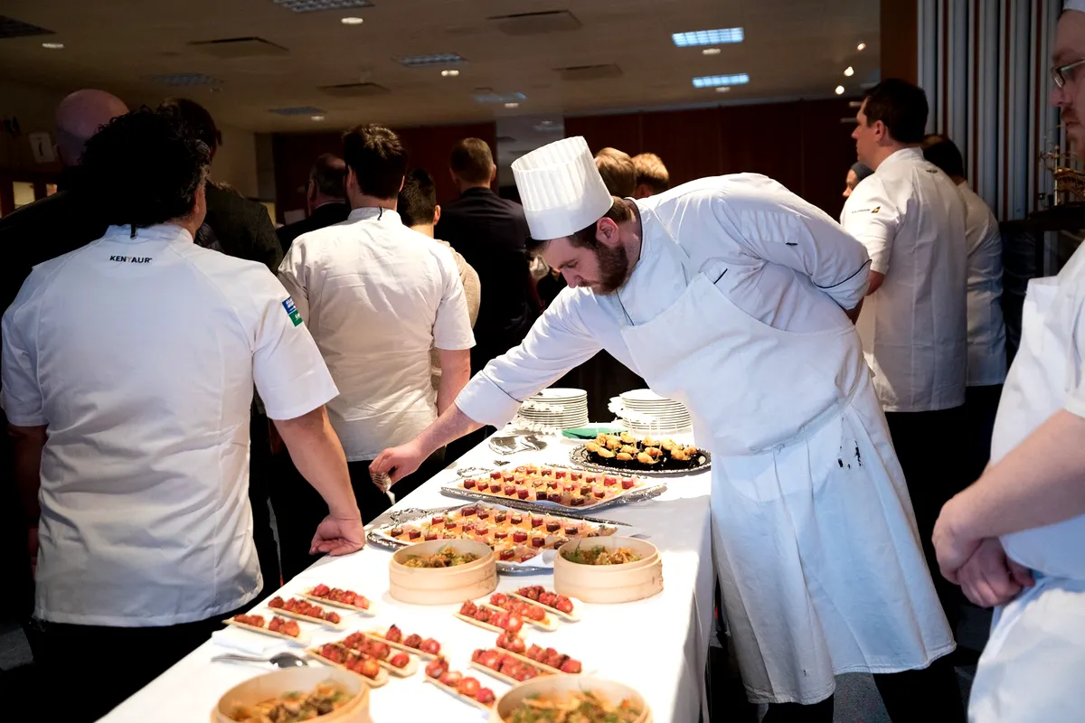 A group of chefs, dressed in white uniforms, preparing and arranging gourmet dishes at the Food and Fun Festival in Iceland.