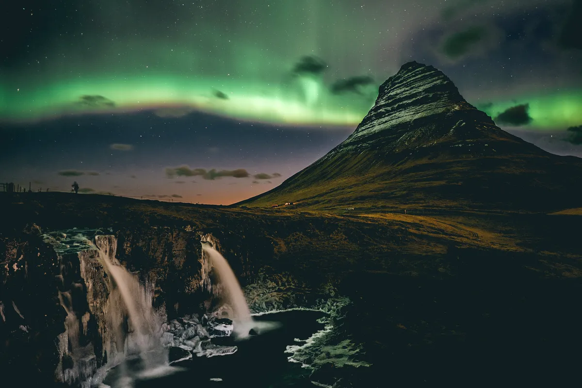 The mesmerizing Northern Lights illuminate the sky above Kirkjufell mountain and its nearby waterfall. The vivid green aurora stretches across the night, creating a mystical scene.