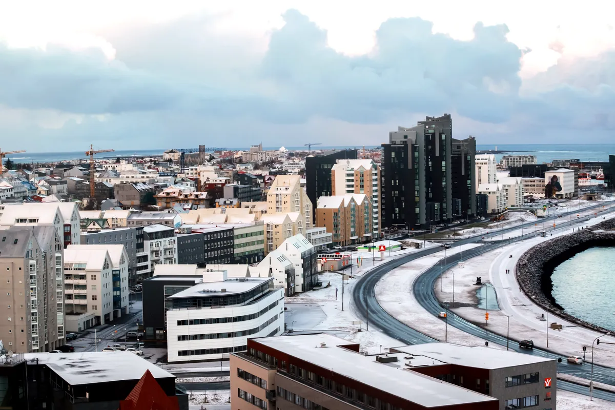 A view of Reykjavik’s skyline with modern buildings, snow-capped rooftops, and the coastline in the distance. The city’s unique blend of architecture and nature is highlighted by the wintery landscape.